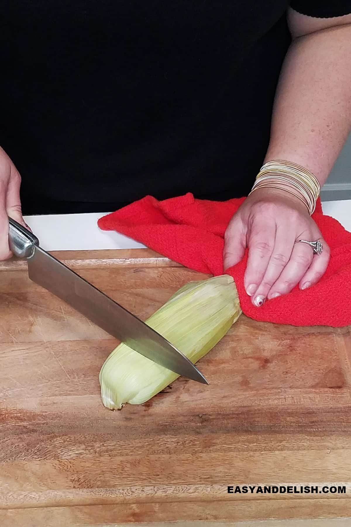 microwaved whole corn on the cob on a cutting board with an end about being cut off.