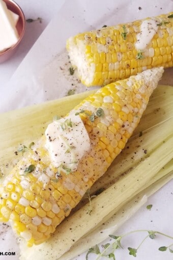 two cooked shucked corn on the cob with a at of butter and some seasonings on top.