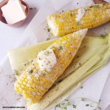 two cooked shucked corn on the cob with a at of butter and some seasonings on top.