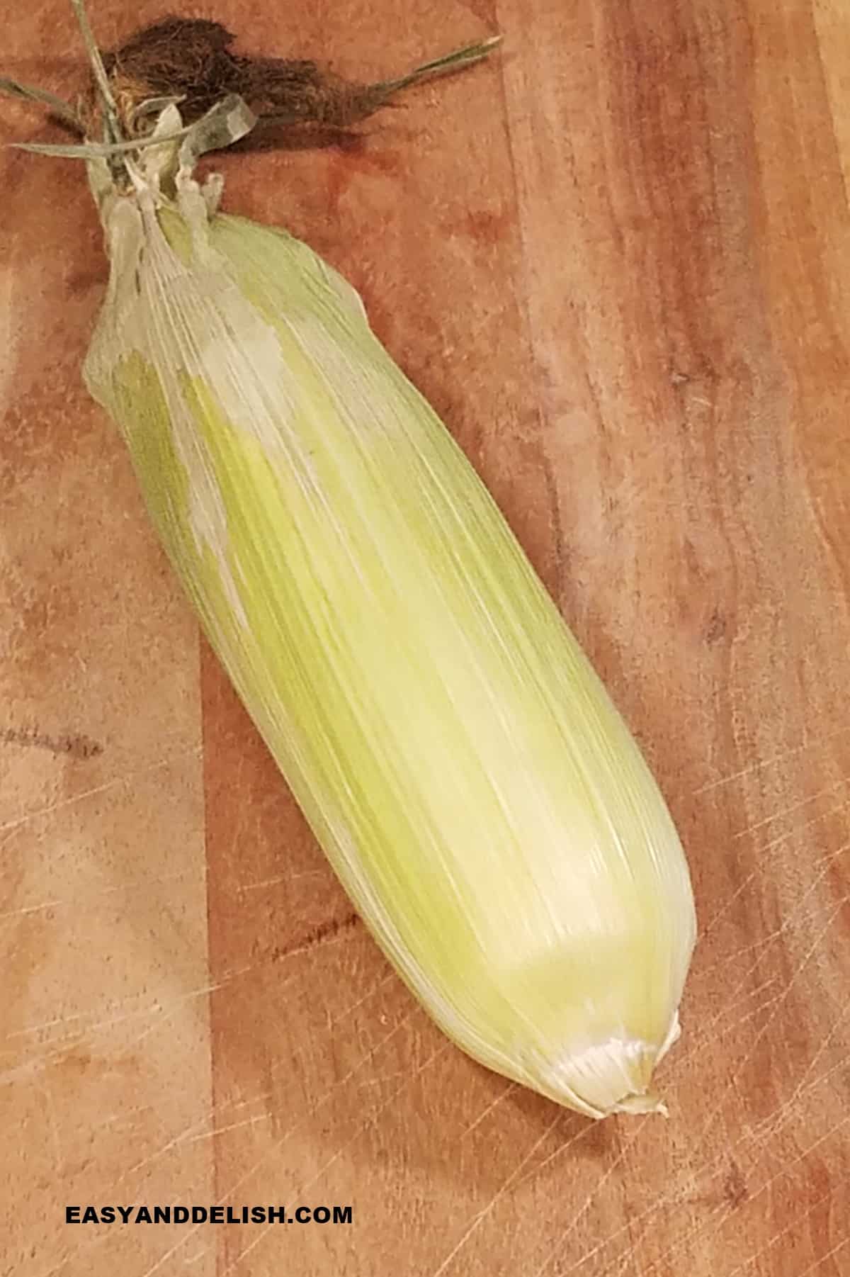 whole unchucked summer vegetable on teh cob on a cutting board.