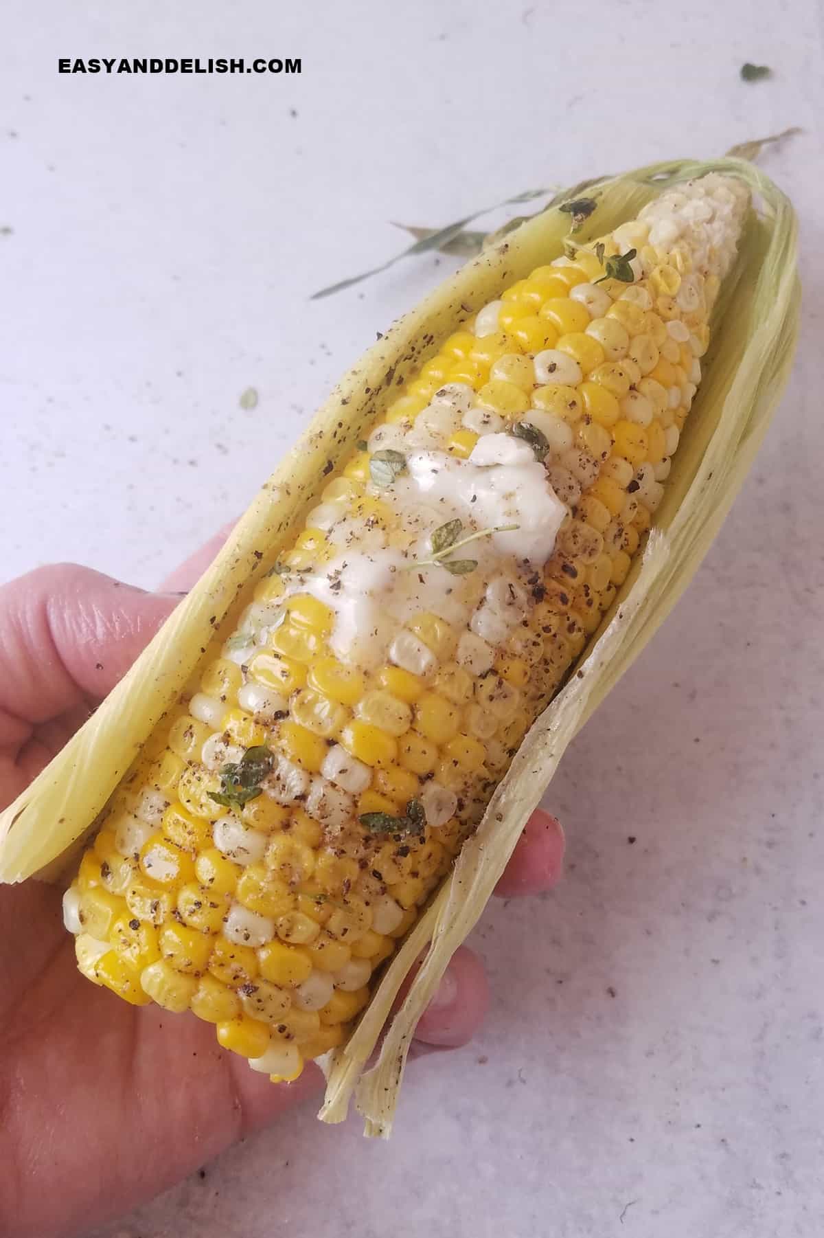 a hand holding an ear of the summer vegetable with butter and seasoning on top. 