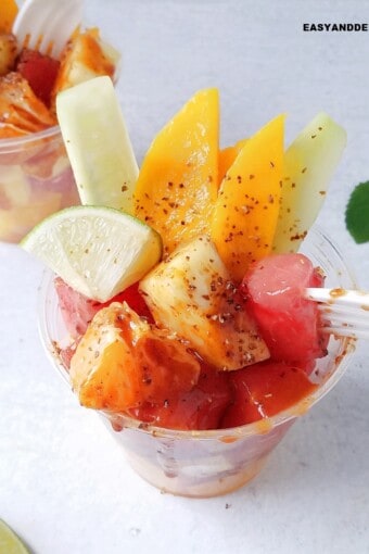 Mexican fruit cups on a table with fresh mint leaves and lime wedges around them.