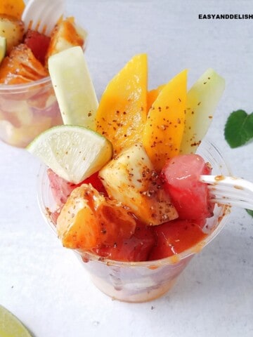 Mexican fruit cups on a table with fresh mint leaves and lime wedges around them.