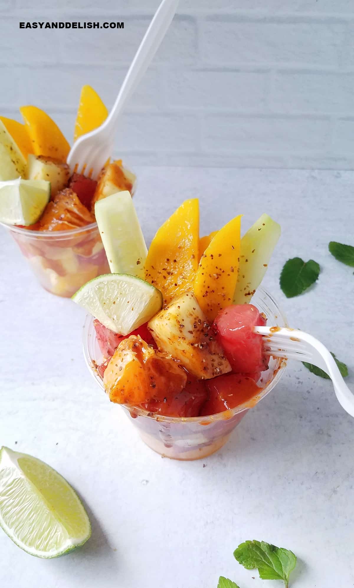 Mexican fruit cups with forks plus garnishes around them on the table.