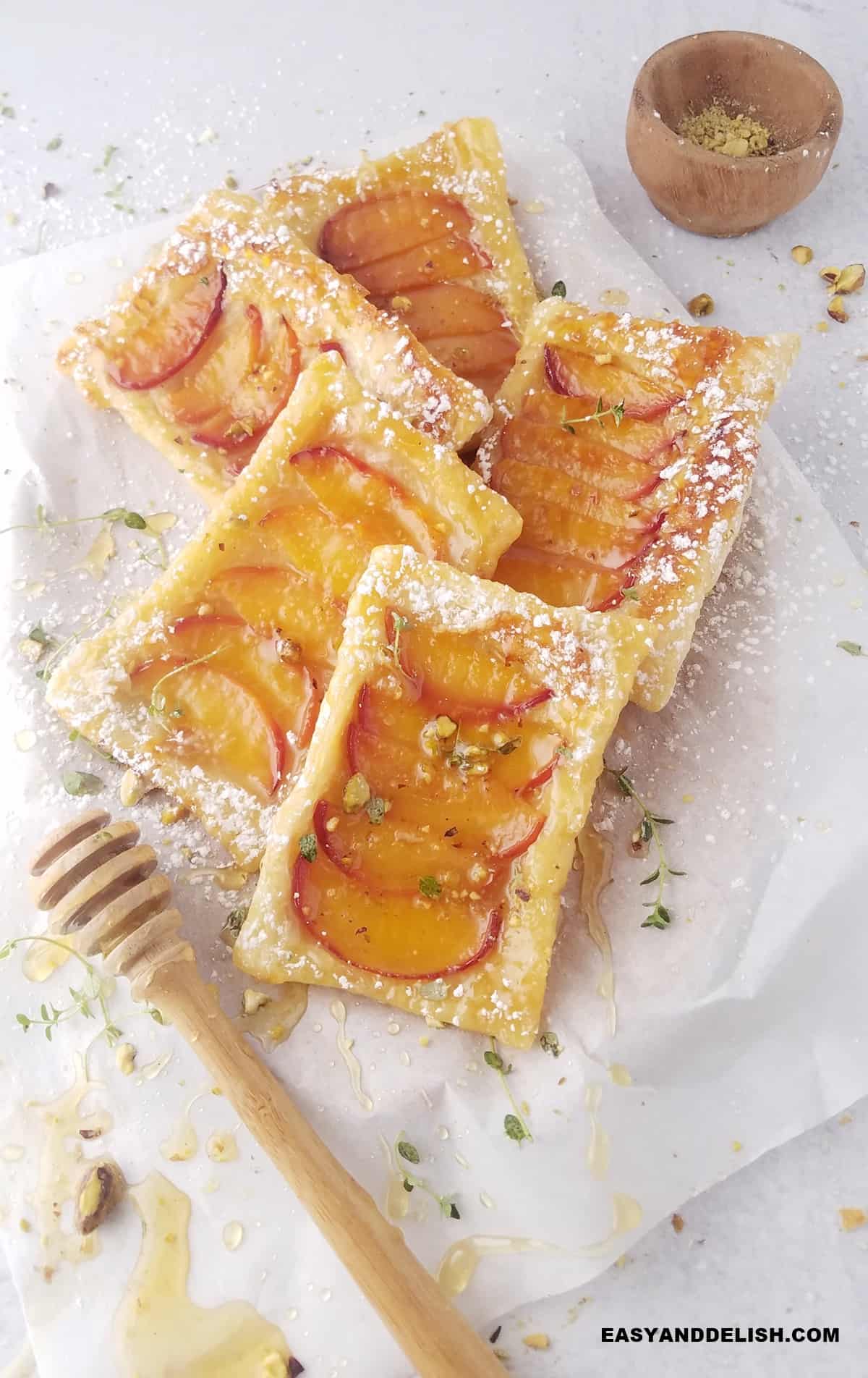 a bunch of puff pastry peach tarts on a tray with nuts and honey around them. 