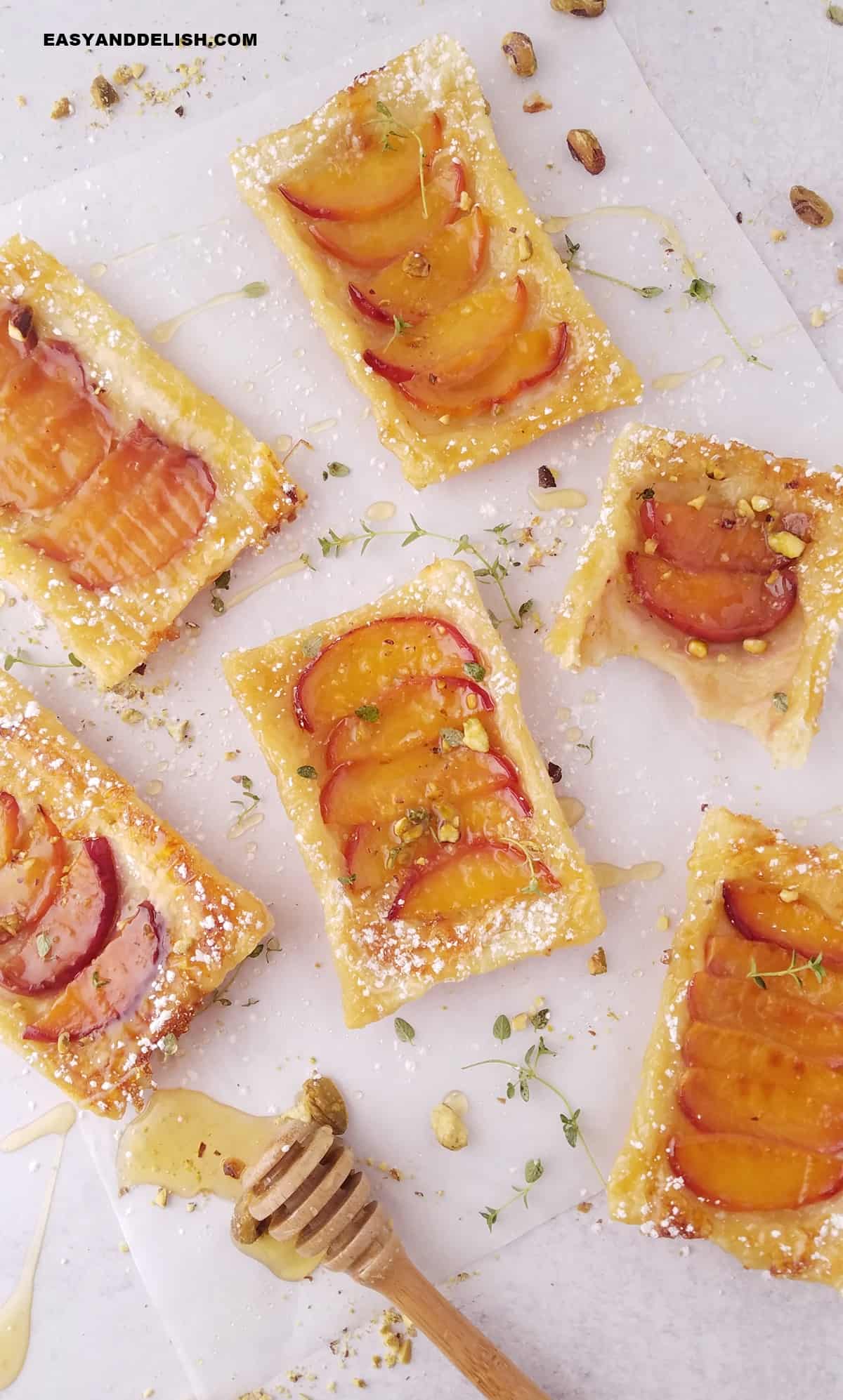 several upside down peach tarts with puff pastry over parchment paper with garnishes sround them. 