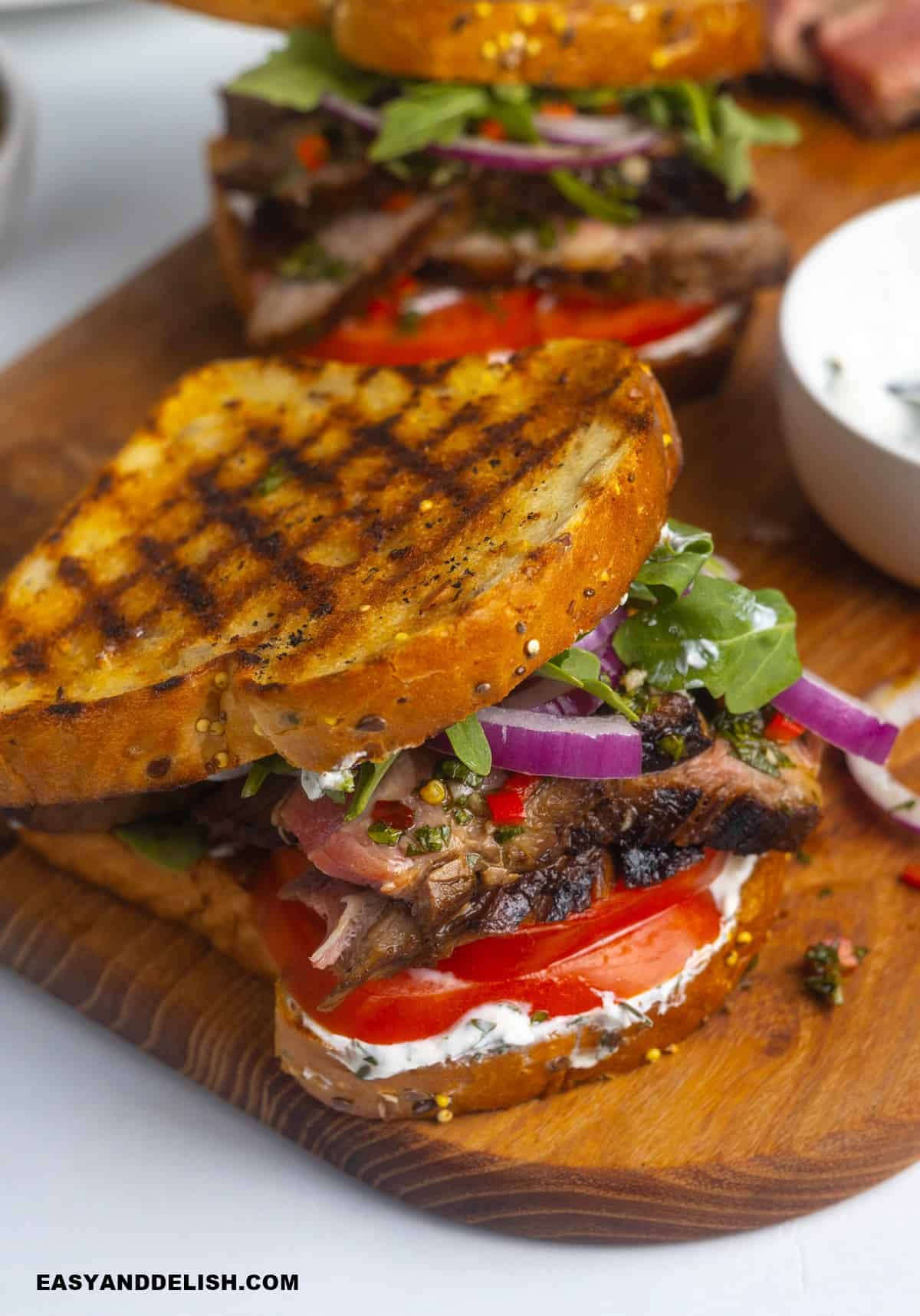 two steak sandwiches on a cutting board.