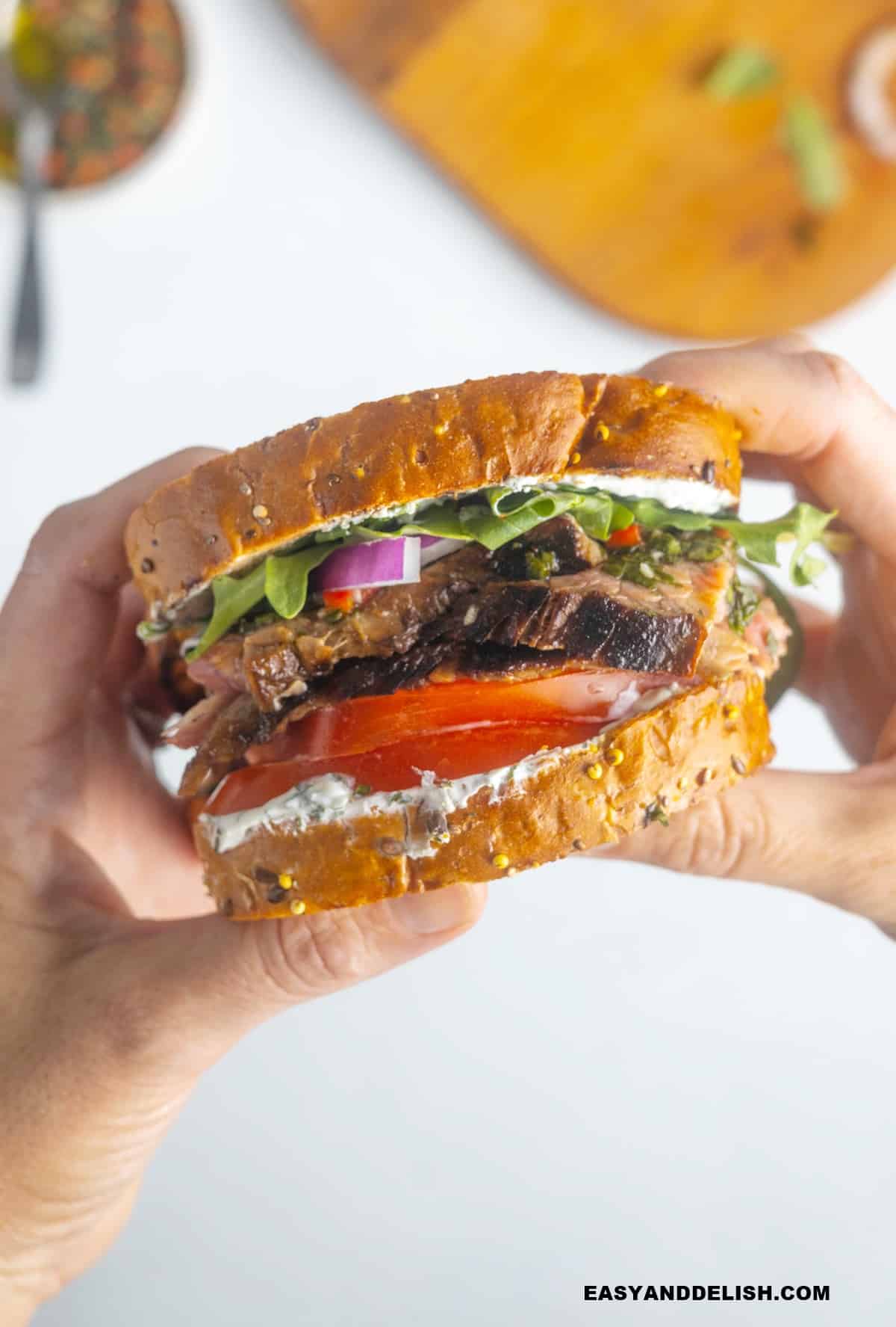 two hands holding flank steak sandwich.