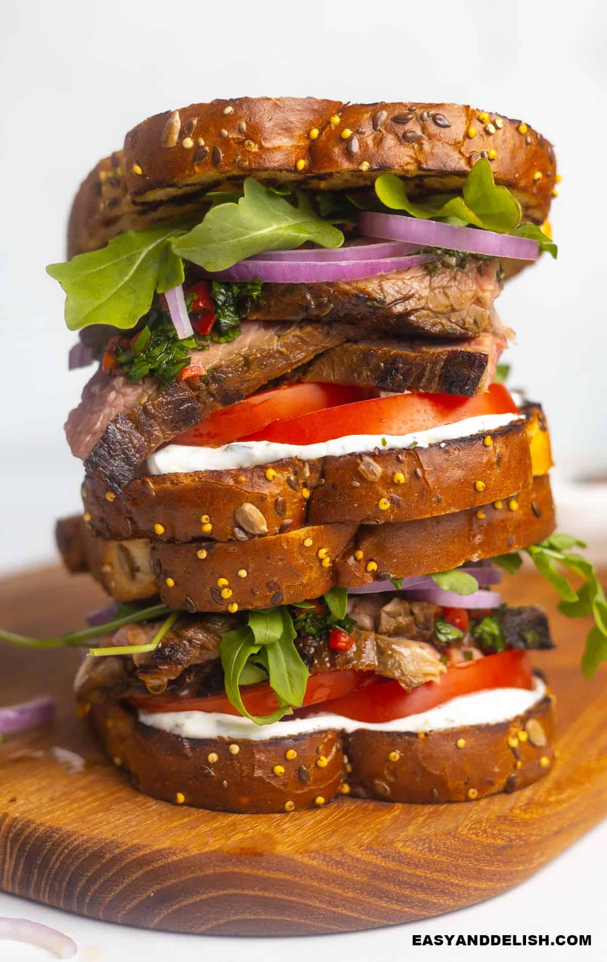 two steak sandwiched piled up on a cutting board.