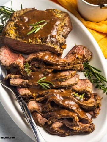 close up of a platter with sliced roast beef topped with bee gravy and garnished with fresh herbs.