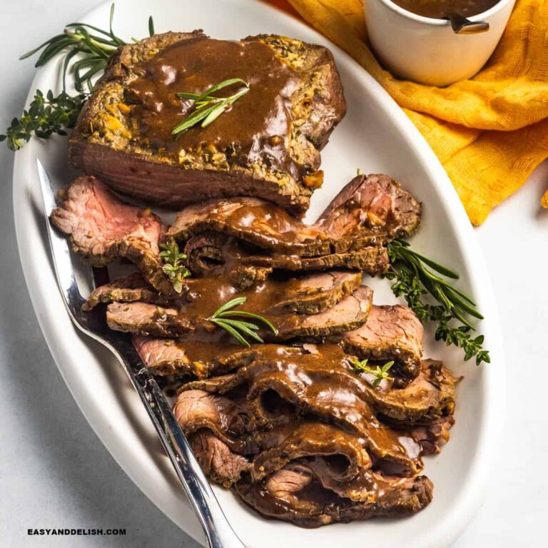 close up of a platter with sliced roast beef topped with bee gravy and garnished with fresh herbs.