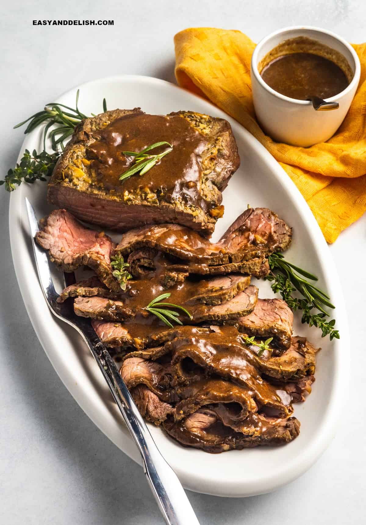 sliced meat in a platter with gravy and herbs.