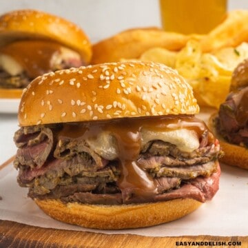 a roast beef sandwich on a cutting board with some other ones on the back.