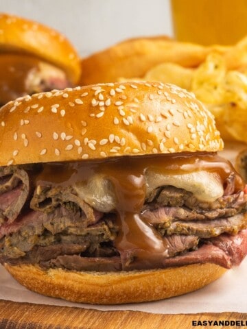 a roast beef sandwich on a cutting board with some other ones on the back.