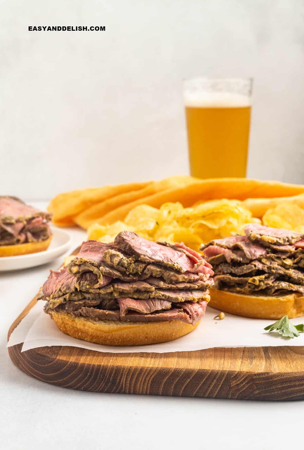 a glass of beer on the background with some roast beef sandwiches being assembled.