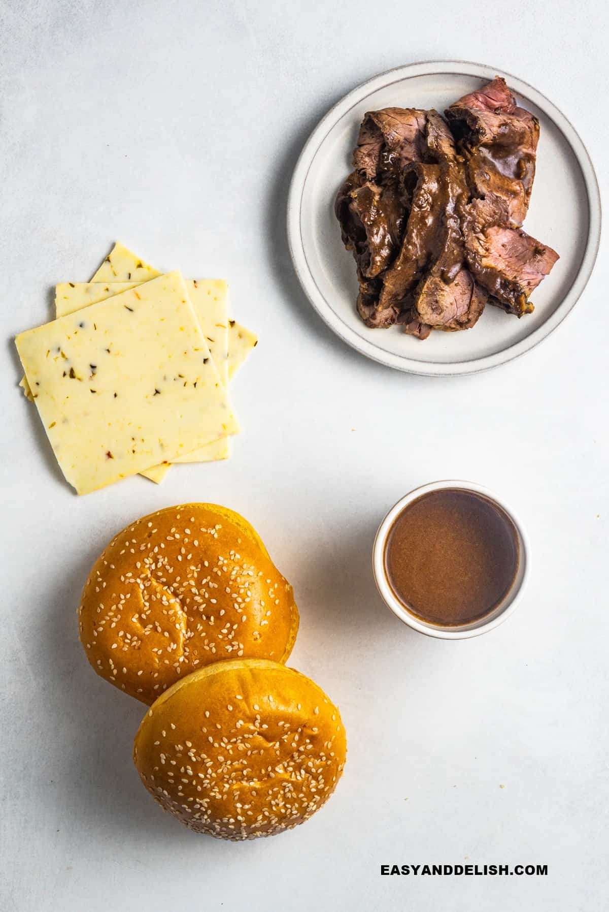 ingredients on a table: meat, buns, gravy, and cheese slices.