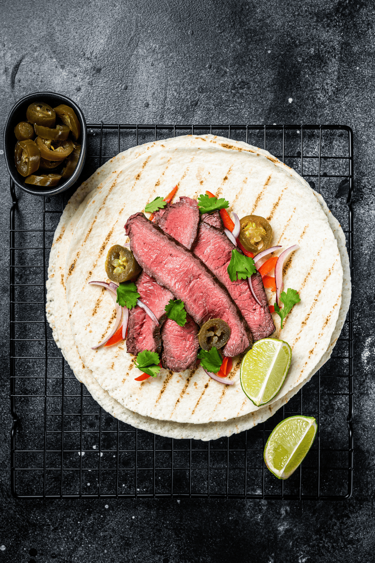 a flank steak taco over a rack with lime wedges and otehr garnish on the side.