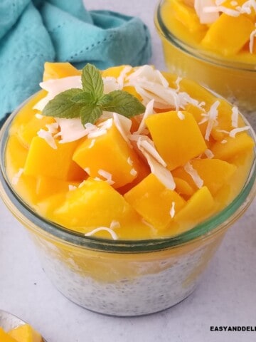 close up of a jar of coconut chia pudding with mango chunks and coconut flakes.