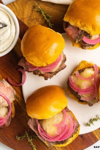 a bunch of roast beef sliders with aioli and herbs on the side.