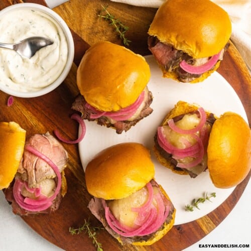 a bunch of roast beef sliders with aioli and herbs on the side.
