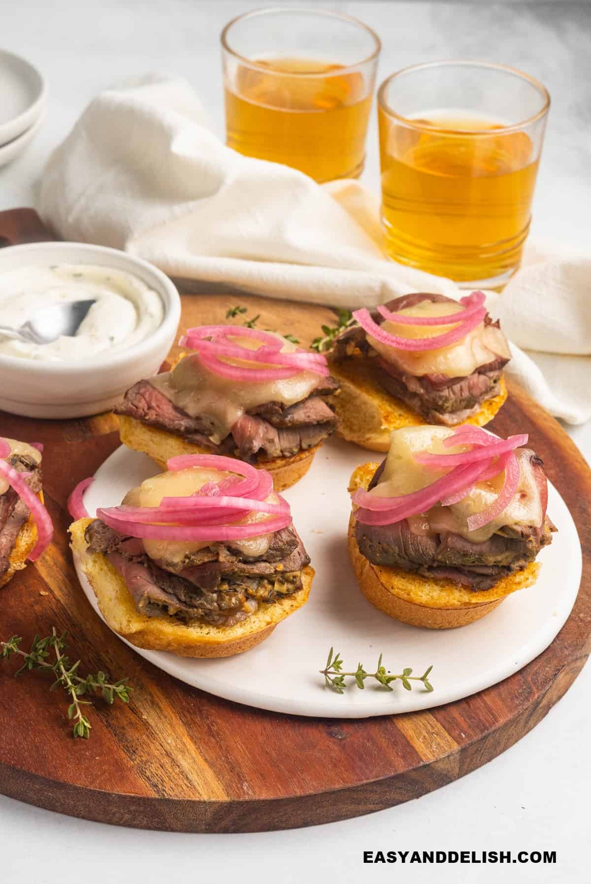 mini sandwiches in a tray with some aioli and beverages on the sides. 