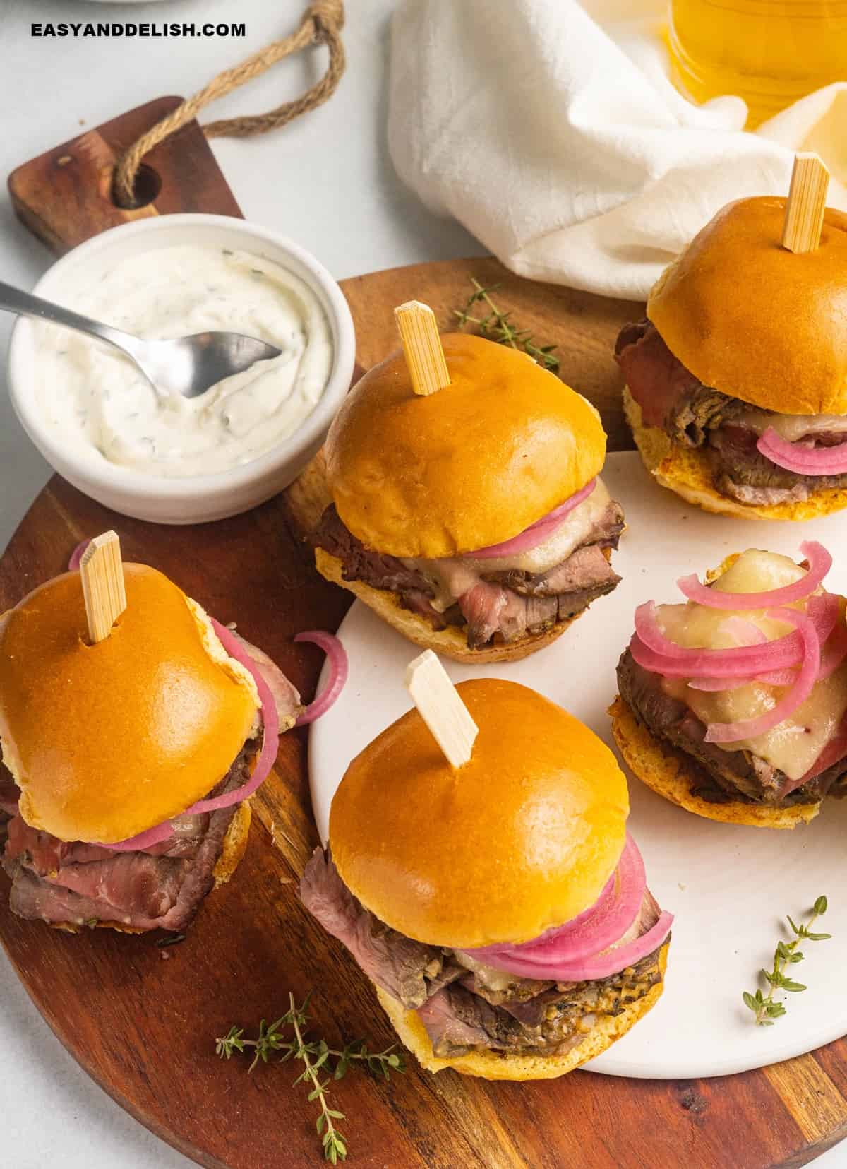 Roast beef sliders in a tray with a bowl of aioli on the side.