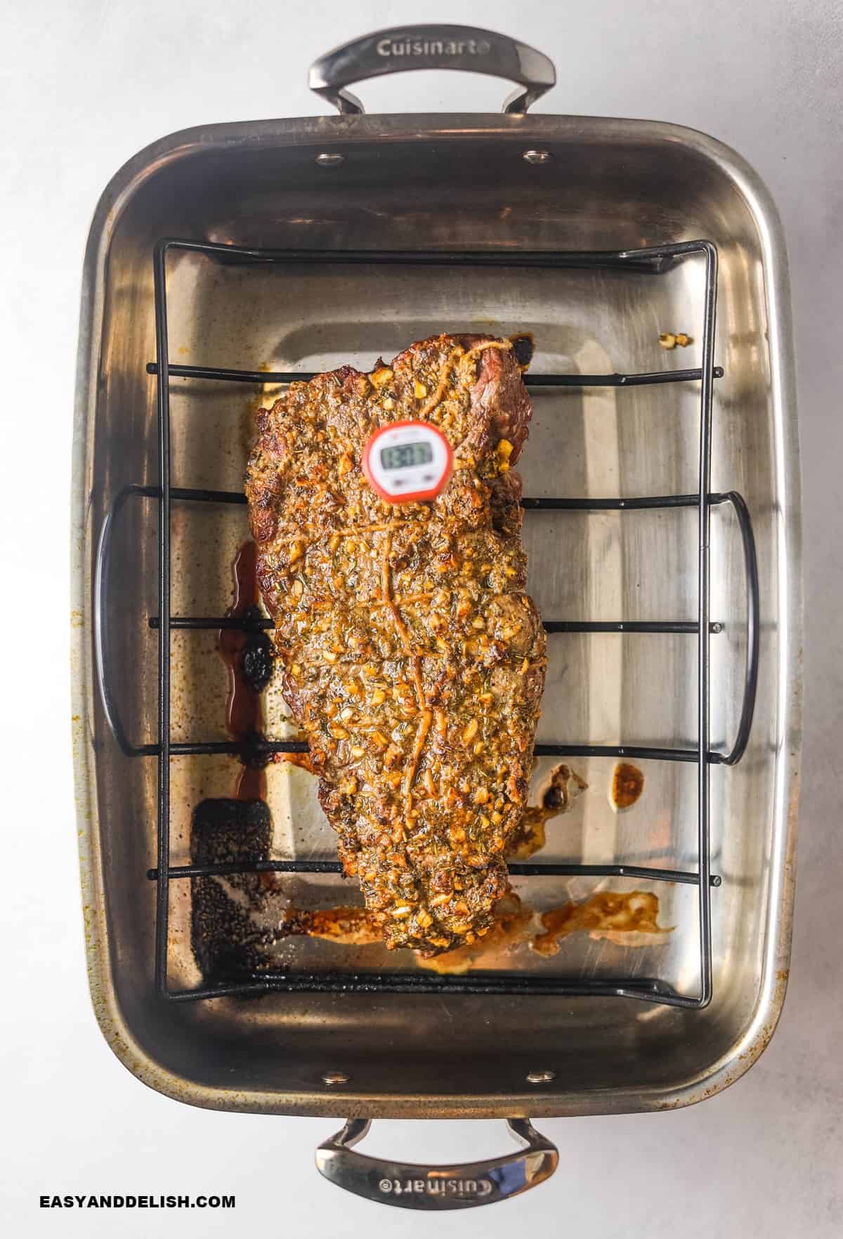 rosbife assado no forno em uma assadeira com um termometro de carne enfiado na parte mais espessa da carne. 