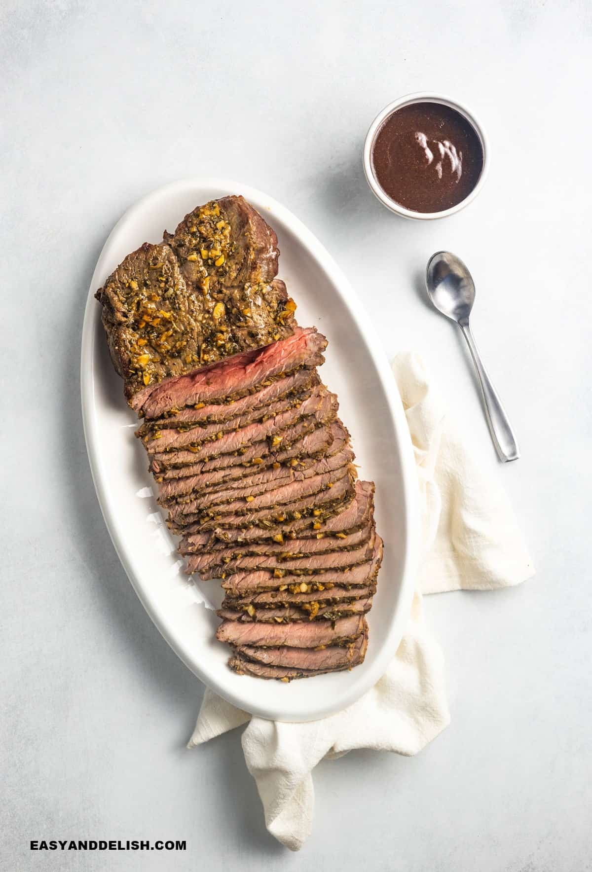 rosbife assado e fatiado ser vido com uma tigela de molho de vinho ao lado. 