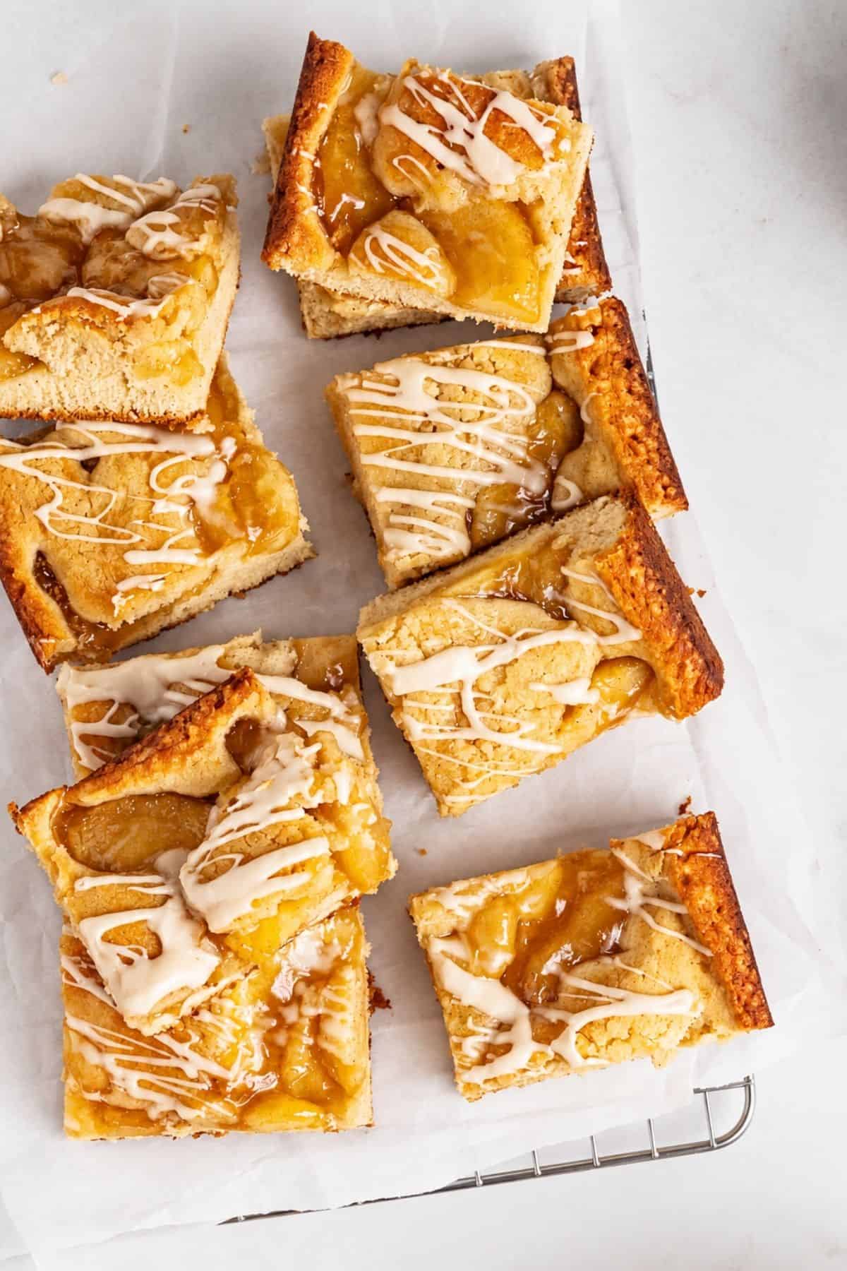 Glazed apple bars on parchment paper over a cooling rack.
