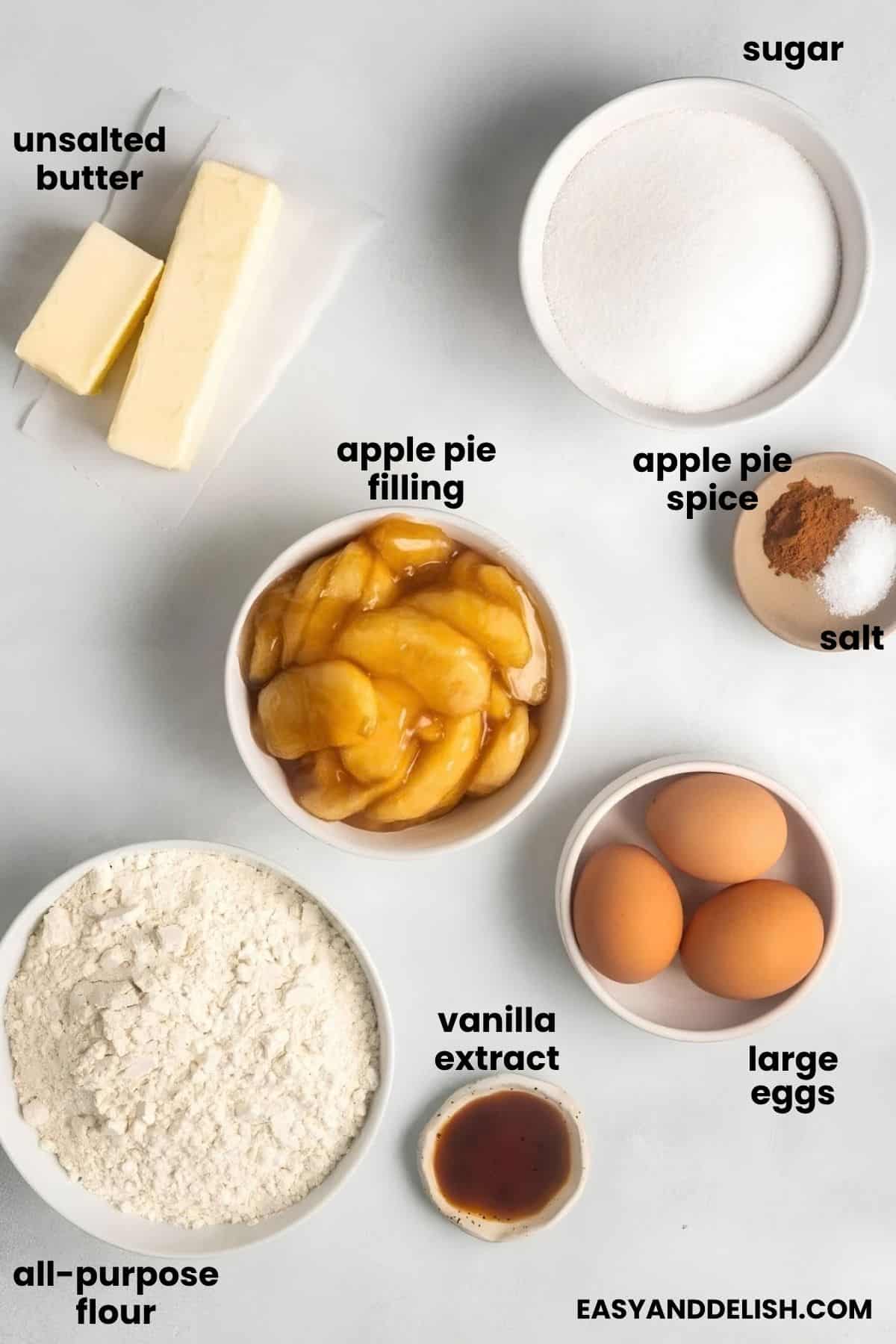 Butter, sugar, flour, eggs, spices, vanilla, and apple pie filling arranged for the recipe.