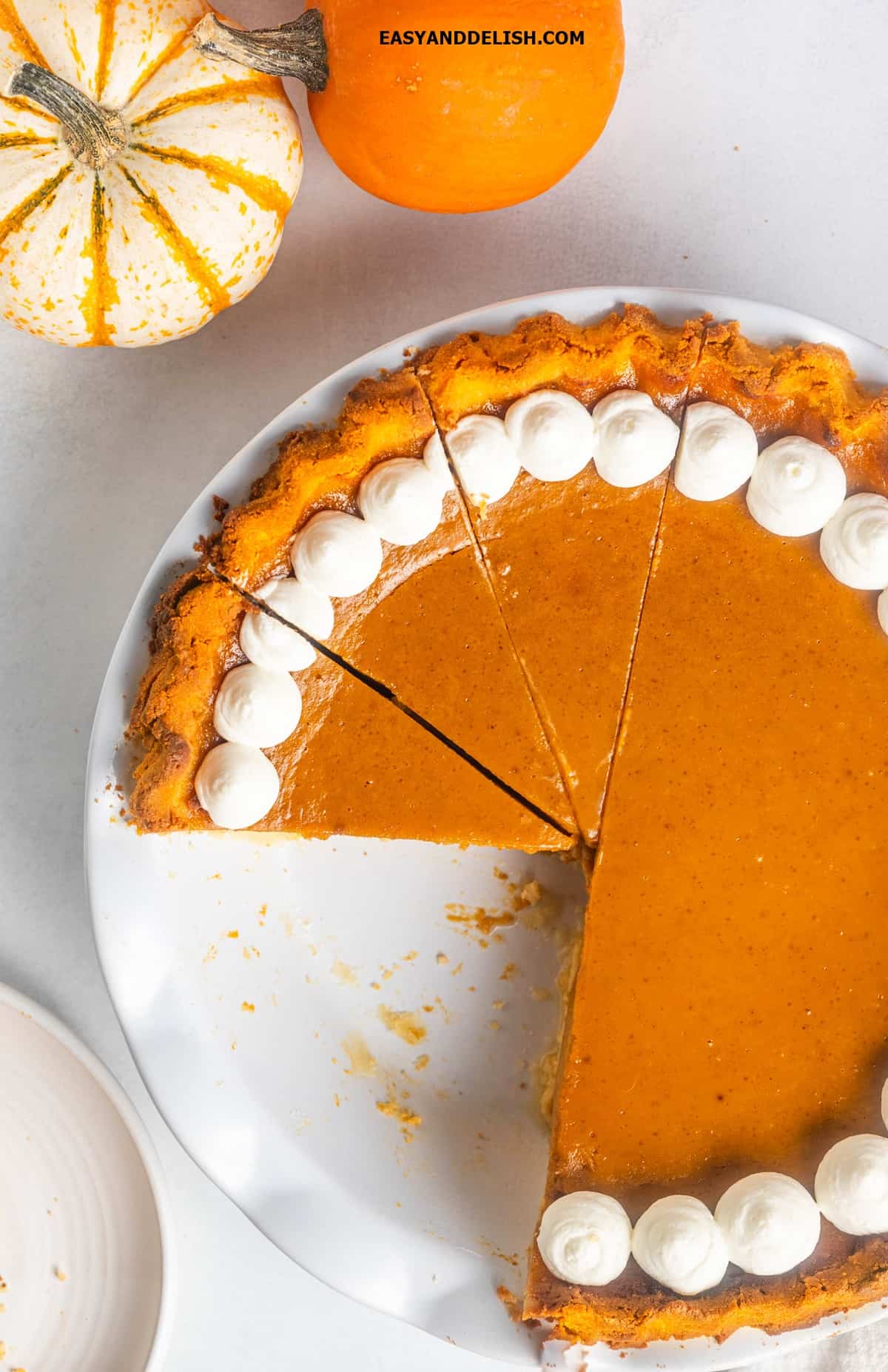 keto pumpkin pie partially sliced in a plate with small pumpkin on the side. 