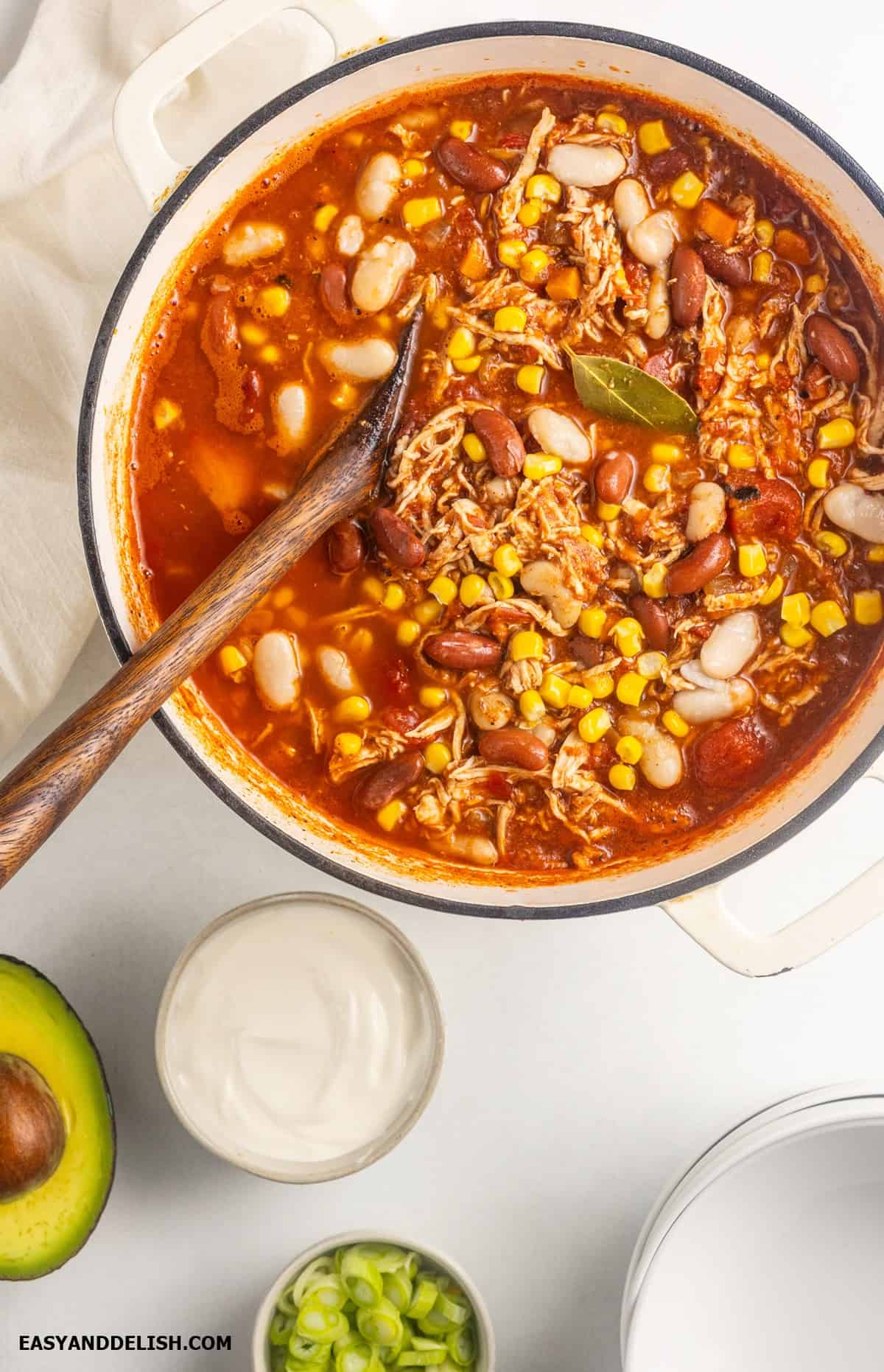 A bowl of red turkey chili with some toppings around the bowl on a table. 