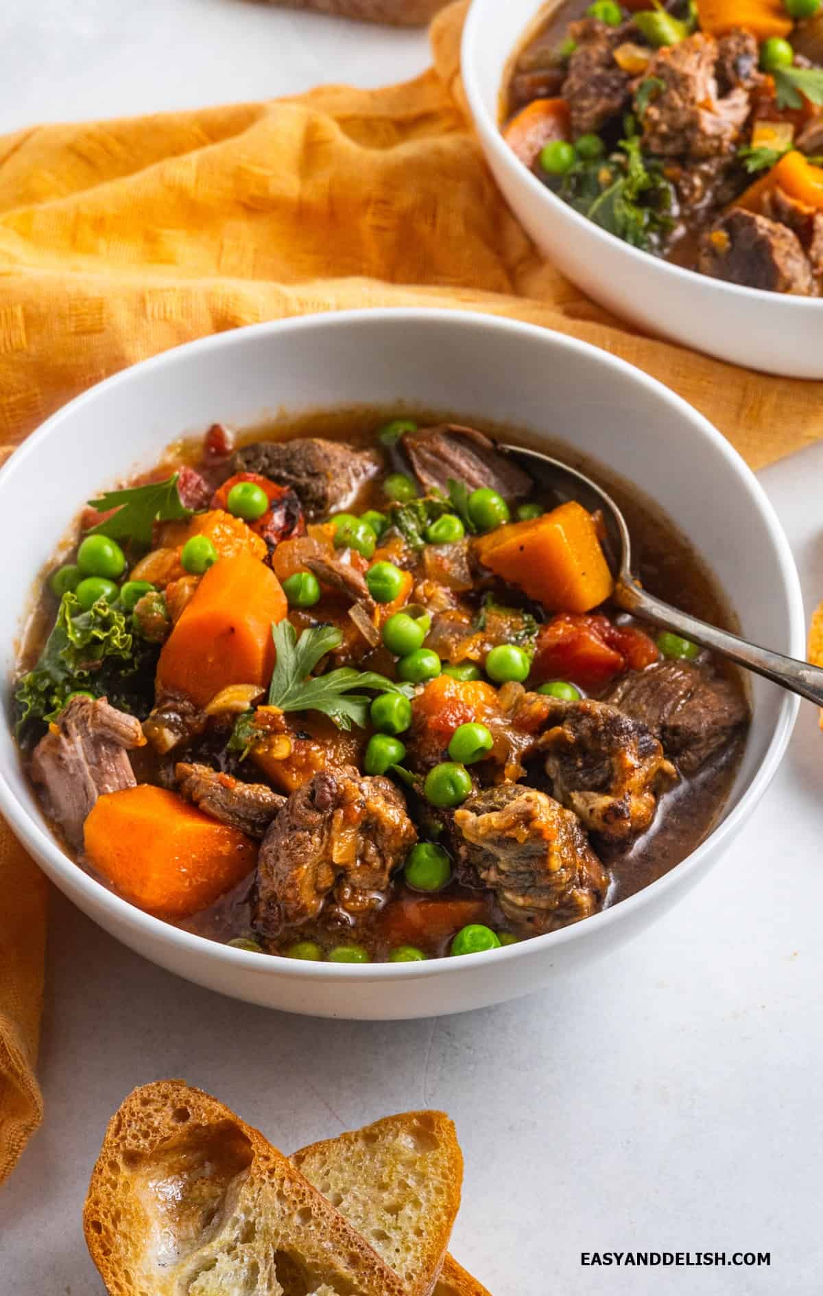 Homemade vegetable beef soup in a bowl with a spoon in it and toasts on the side. 