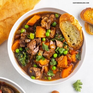 A bowl of vegetable beef soup with a bread toast on top.