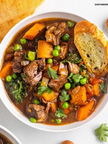 A bowl of vegetable beef soup with a bread toast on top.