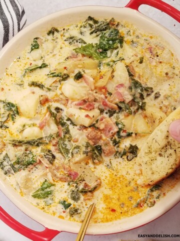 A piece of toast dipped in a bowl of Olive Garden Zuppa Toscana Soup.