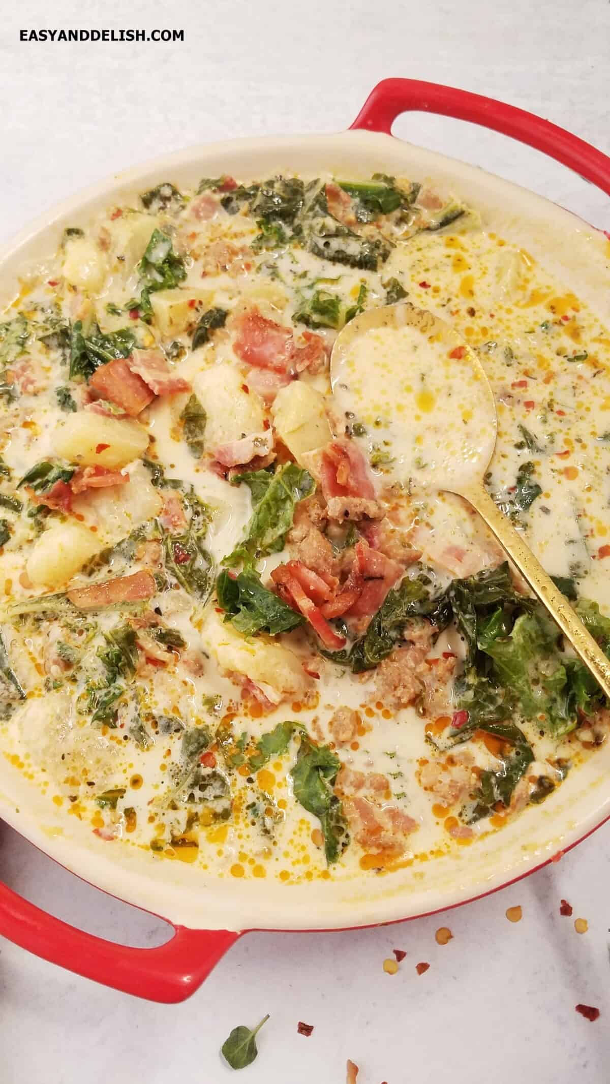 A bowl of hot food with kale, cream, potatoes, spicy Italian sausage, and bacon.