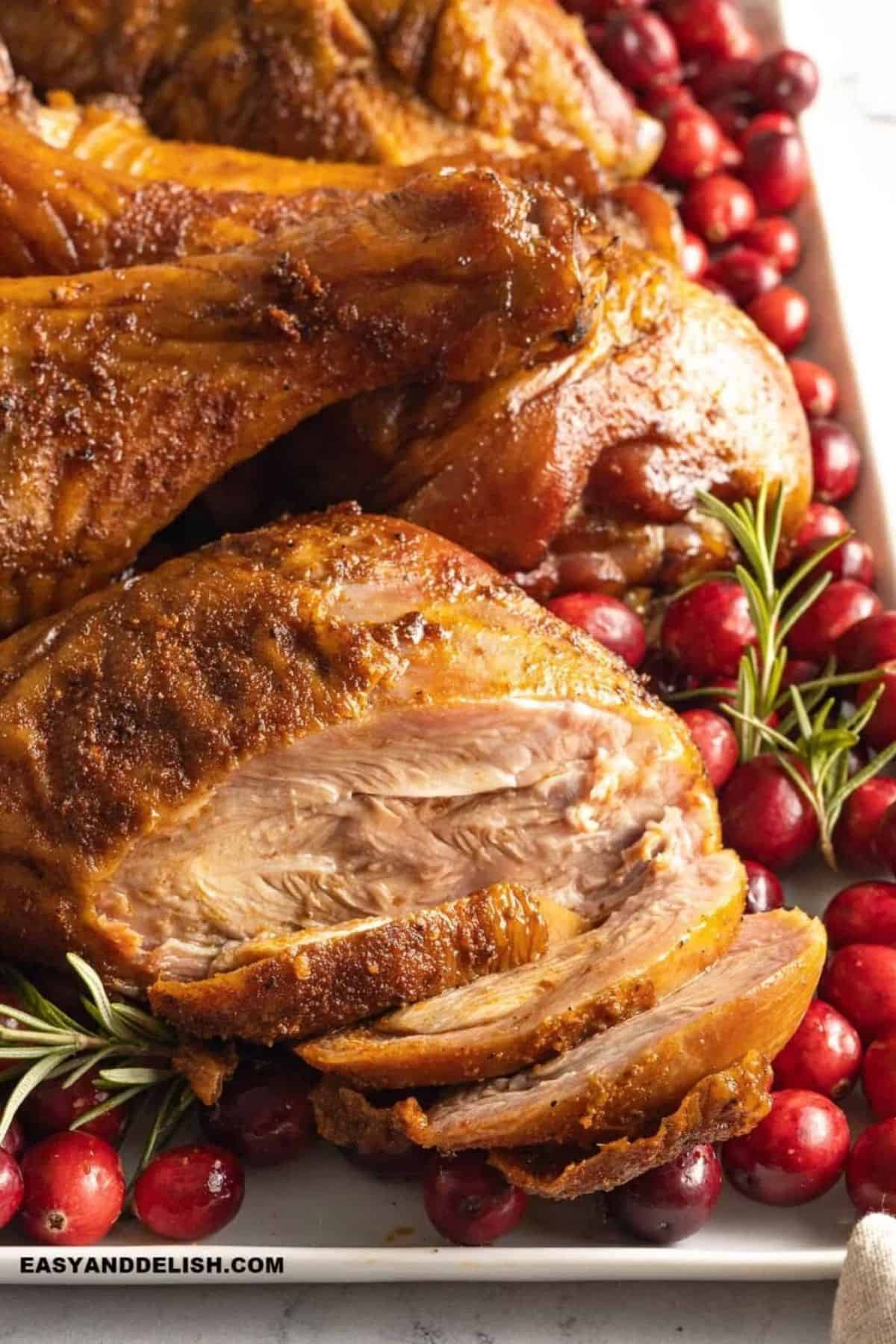 Sliced turkey leg showing tender smoked meat surrounded by cranberries and rosemary.