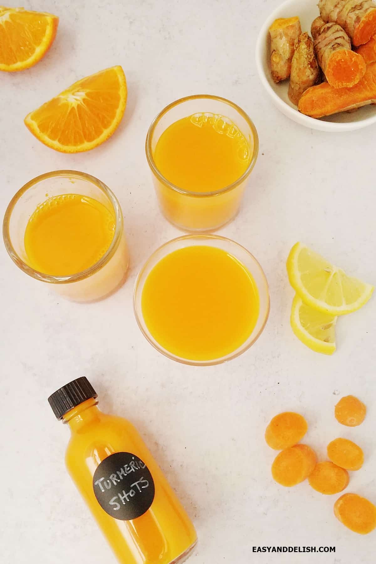 Several turmeric shots in glasses with some ingredients around them. 