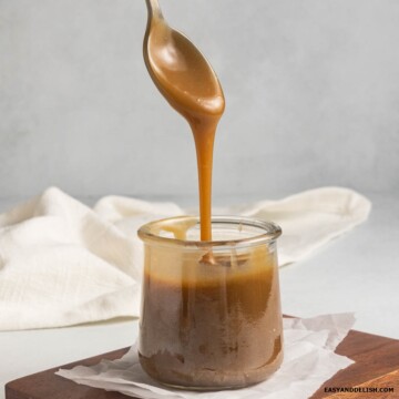 A spoonful of vegan caramel sauce poured into a glass jar.