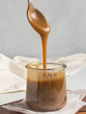 A spoonful of vegan caramel sauce poured into a glass jar.