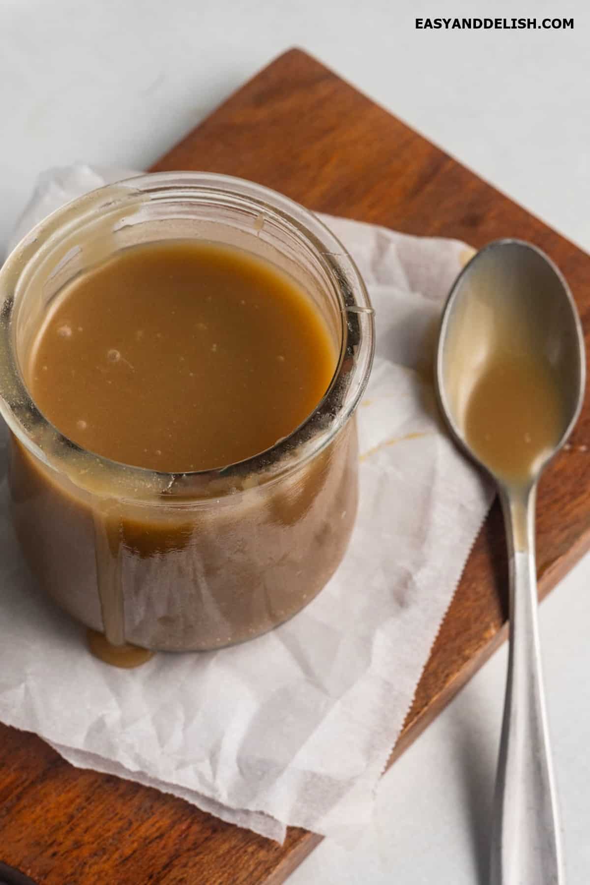 A jar of vegan caramel on a table with a spoon on the side. 