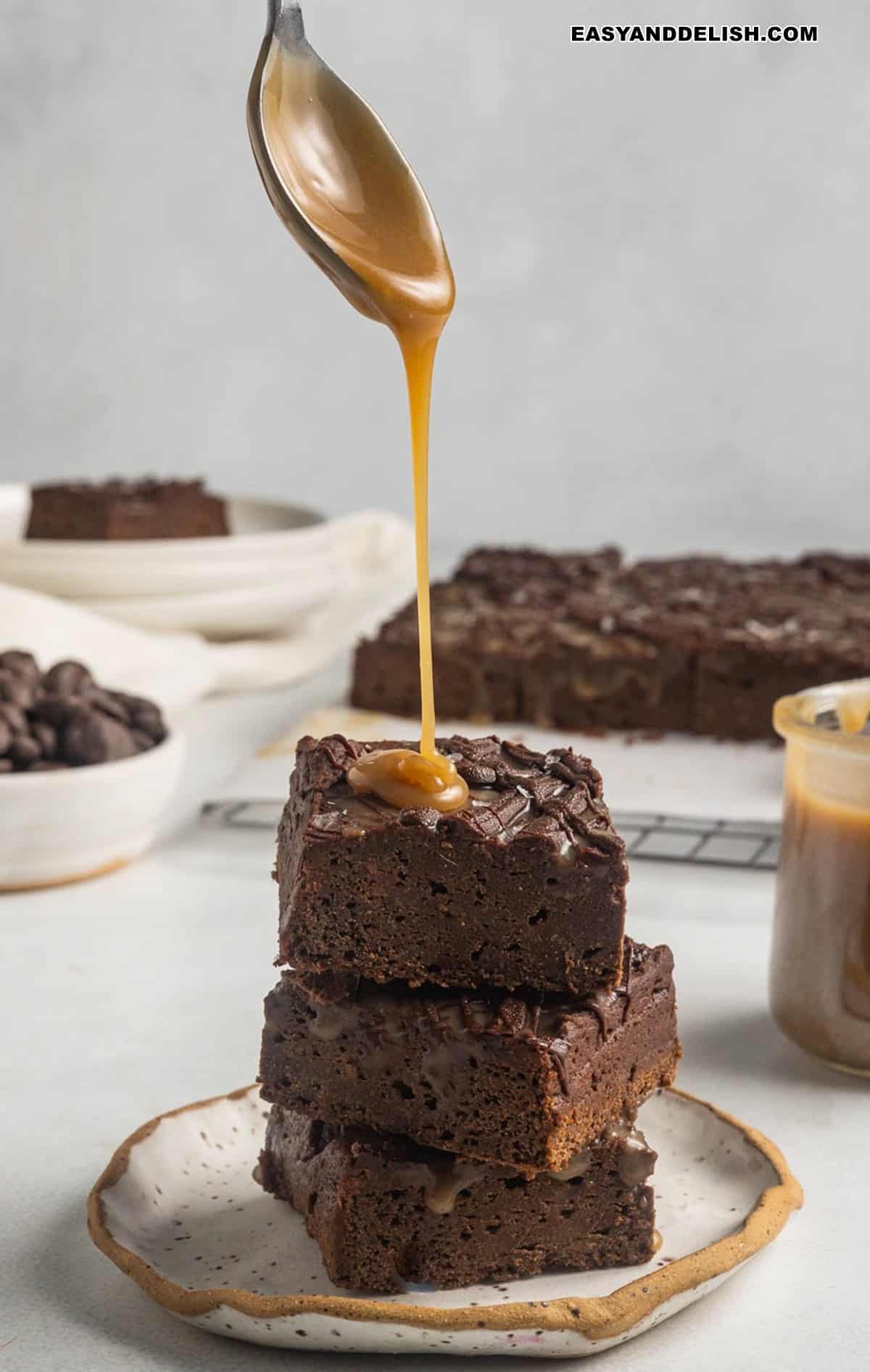 Vegan caramel sauce spooned over a stack of vegan brownies.