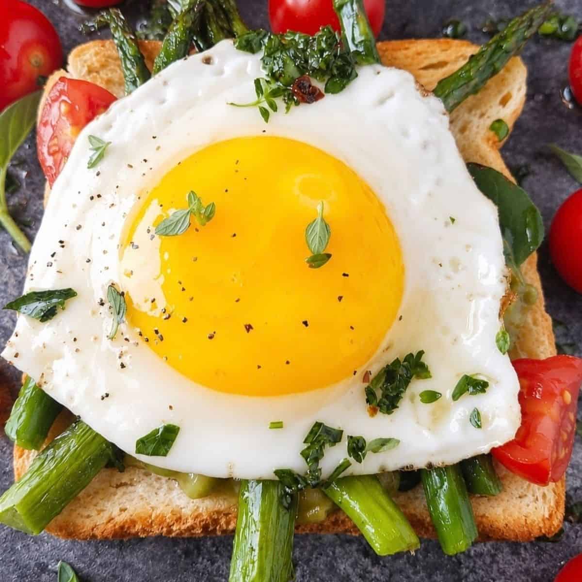 Fried egg served over asparagus and toast with tomatoes and fresh herbs.