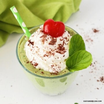 A glass of homemade shamrock protein shake topped with whipped cream, chocolate shavings, and a cherry.