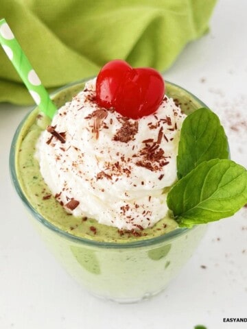 A glass of homemade shamrock protein shake topped with whipped cream, chocolate shavings, and a cherry.