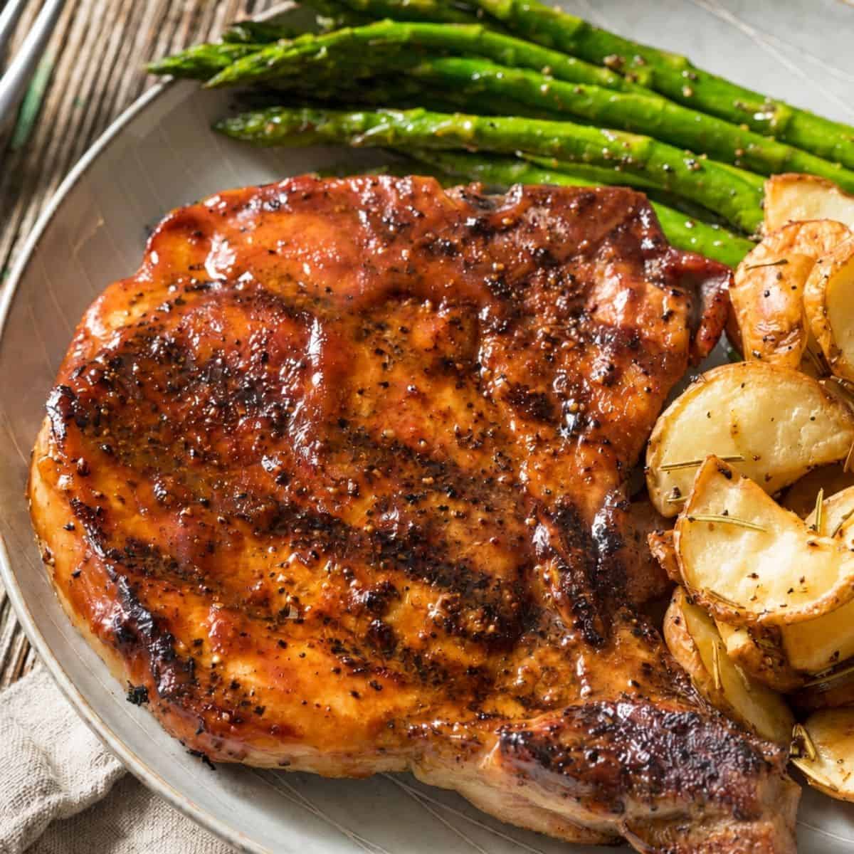 Glazed pork chop served with roasted potatoes and asparagus.