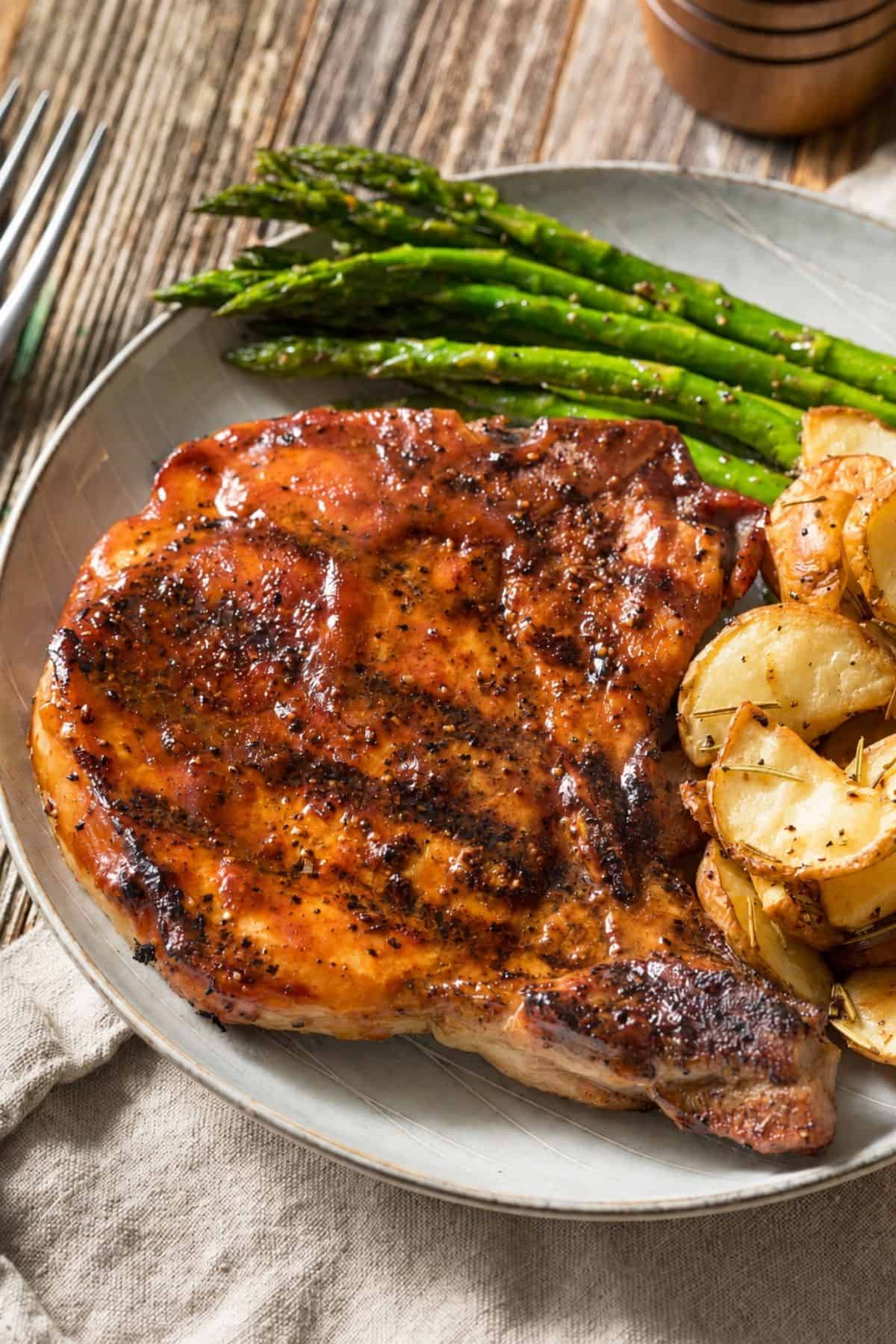 Griddled pork chop served with asparagus and roasted potatoes.