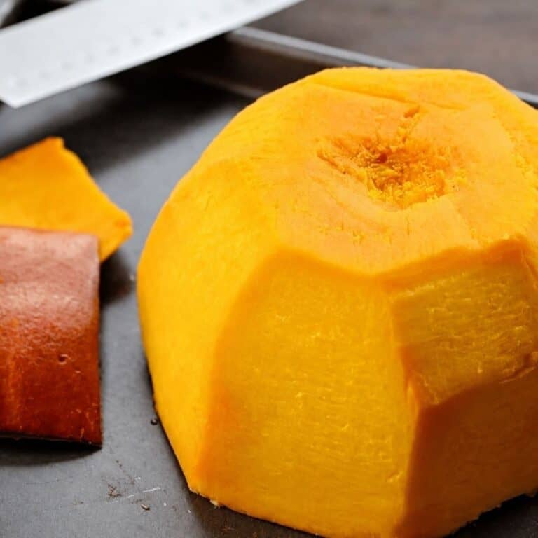 Bright yellow-orange pumpkin flesh with pieces of removed skin on a dark metal baking sheet.