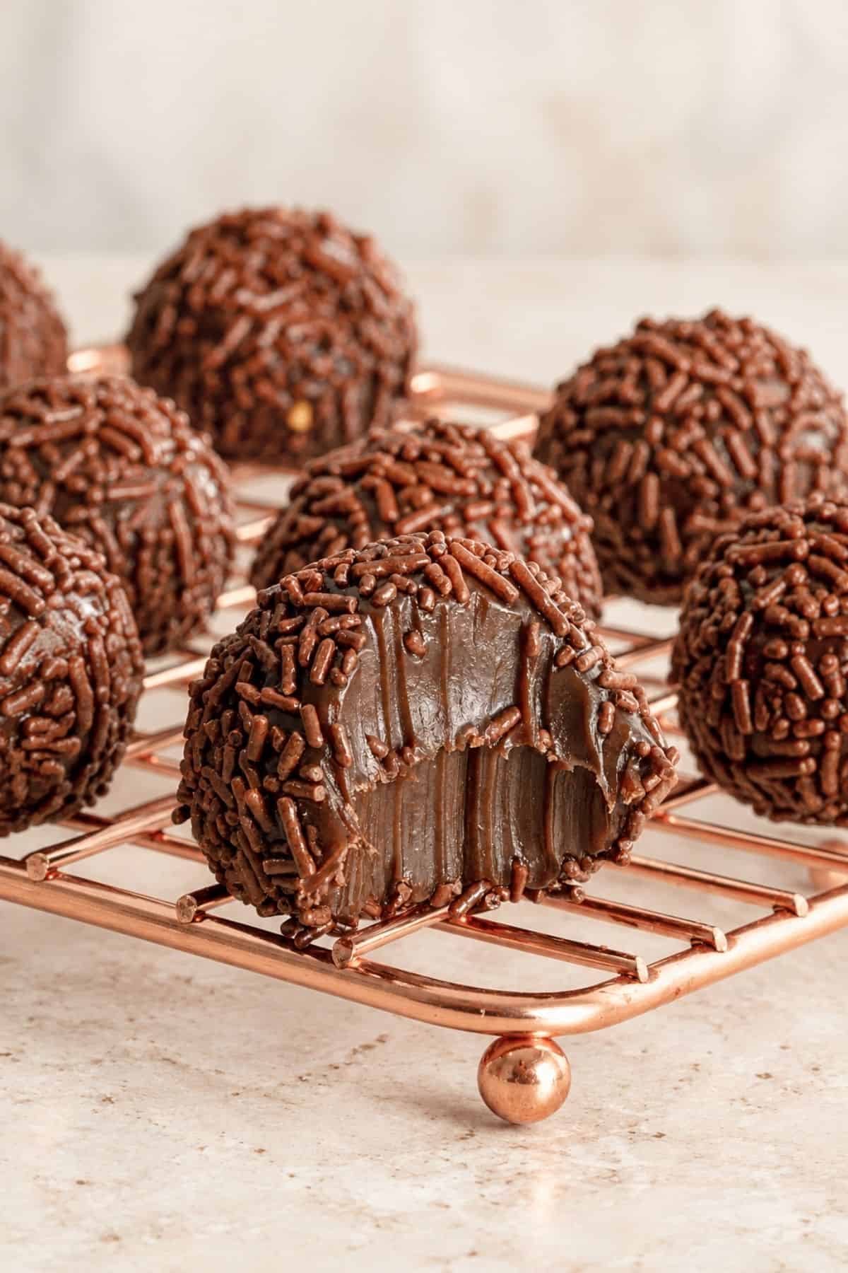 Cut-open brigadeiro revealing a fudgy chocolate center, with sprinkle-coated candies in the background.